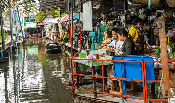 Couple eating next to a boat and small shops and restaurants in Bang Nam Phueng Floating Market