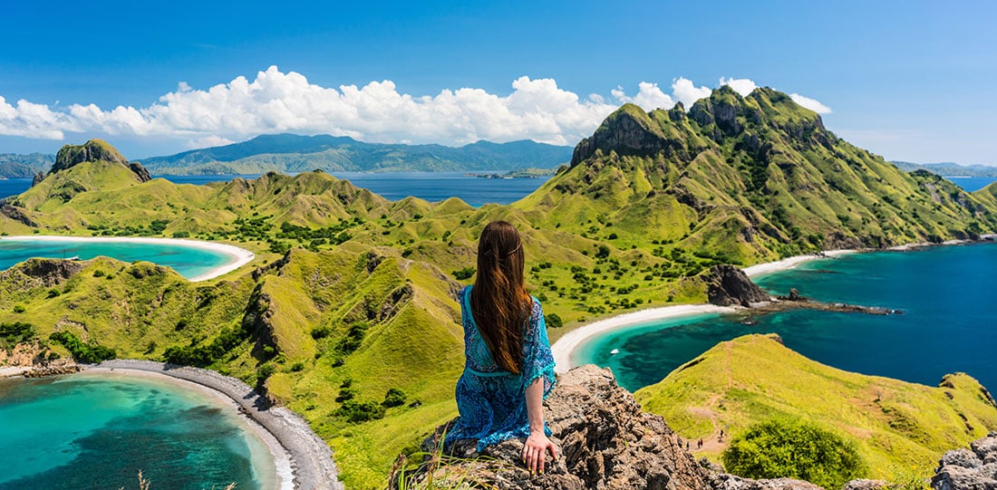 Young woman enjoying the view of Padar Island, while sitting on the top of a volcanic mountain