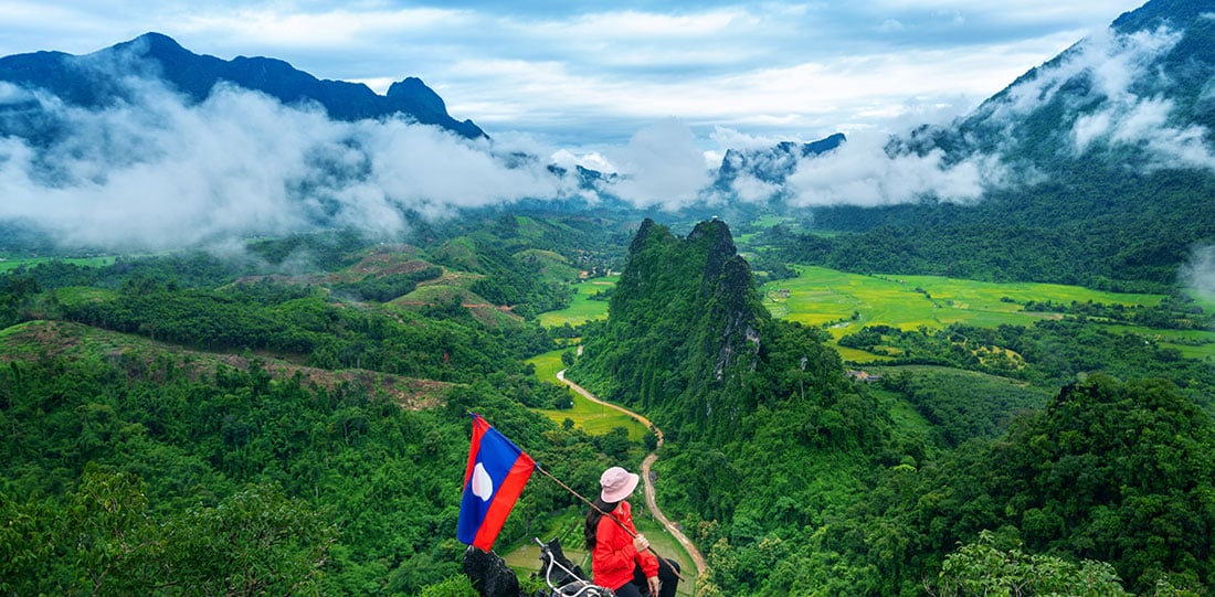Girl with a Laos flag watching out over mountains in Laos
