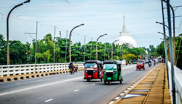 Multicolored tuk-tuks riding on the road from Kalutara with the background of a Buddhist temple.