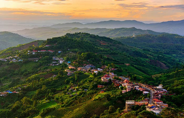 Aerial view of Mae Salong village nestled at the foot of Doi Mae Salong mountain in Chiang Rai, Thailand, with rolling green hills and morning mist.