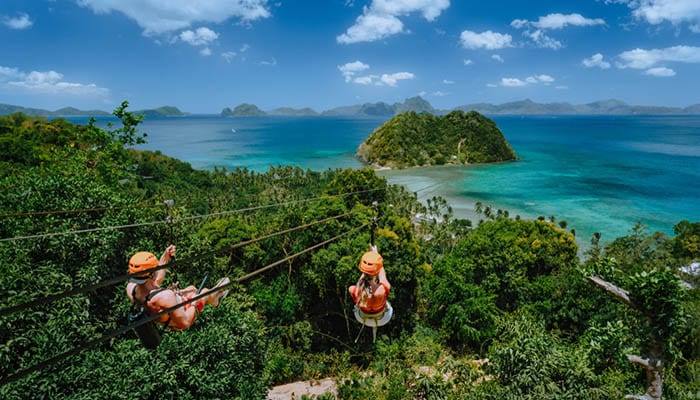 Zipline over Las Cabanas Beach with tourist on sunny day with white clouds over sea. El Nido, Palawan, Philippines