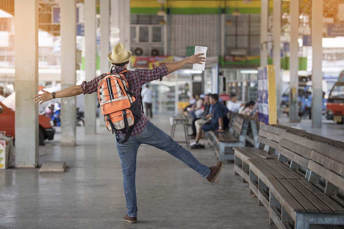Ein aufgeregter Mann mit einem Koffer steht an einem Busbahnhof in Phuket, Thailand, hält eine Karte in der Hand und wartet gespannt auf einen Bus nach Bangkok.