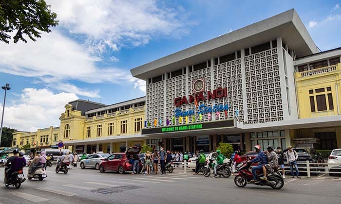 Busy crowded street in front of Hanoi Central Railway Station under a blue sky with a few clouds, dated May 28, 2023.