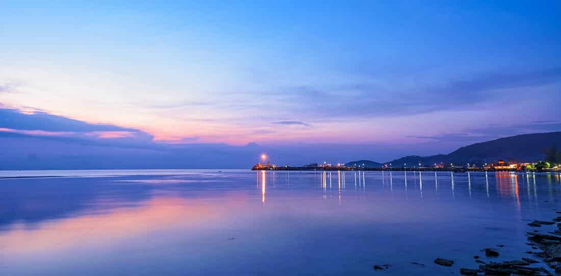Image of Nathon Pier at Ko Samui Island in a serene twilight, with a solitary boat and the colorful sky reflecting on the calm sea surface.